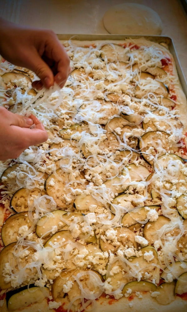 Eine Auberginen-Pizza wird mit Zwiebeln belegt